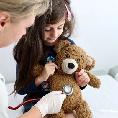 Stuffed bear getting heart listened to by female pediatrician.